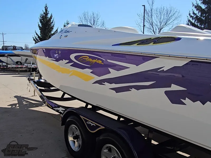 Slide: The Image of 2004 Baja 25 Outlaw boat with vibrant purple and yellow graphics on a trailer. - 25