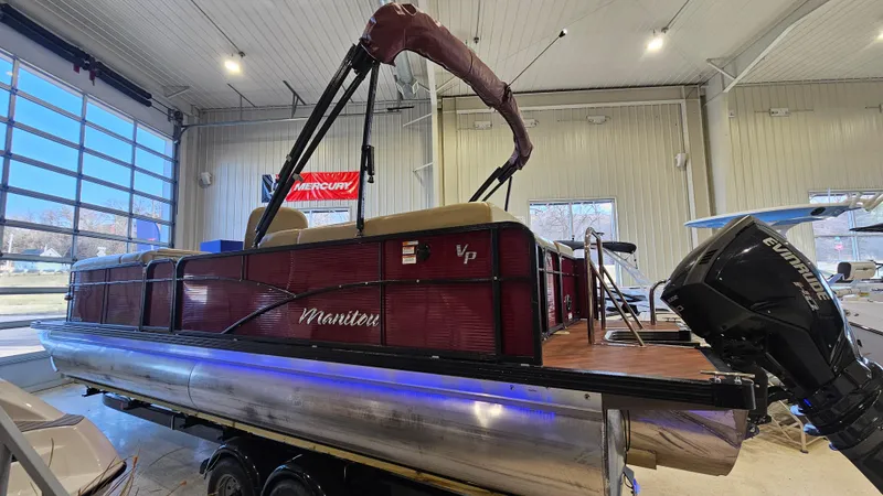 Slide: The Image of 2017 Manitou 25 Aurora LE pontoon boat in showroom, featuring maroon exterior and outboard motor. - 2