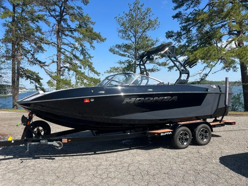 Slide: The Image of 2022 Moomba Mojo boat on trailer, parked near a lake with trees in the background. - 1