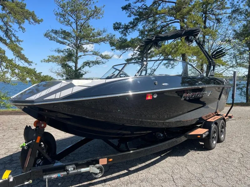 Slide: The Image of 2022 Moomba Mojo boat on trailer, parked near a scenic lake with trees. - 2