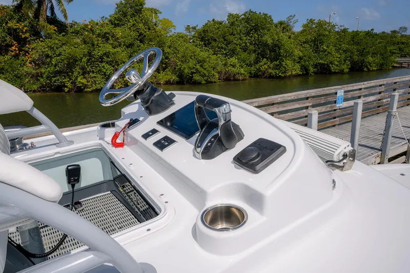 Slide: The Image of Helm of 2024 Freeman 28 boat with steering wheel and controls, docked by lush greenery. - 25