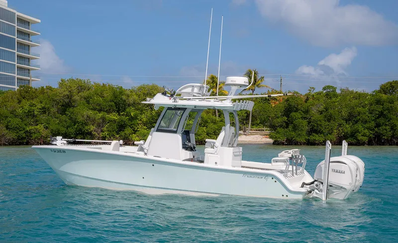 Slide: The Image of 2024 Freeman 28 boat on clear water near lush greenery and modern building. - 28