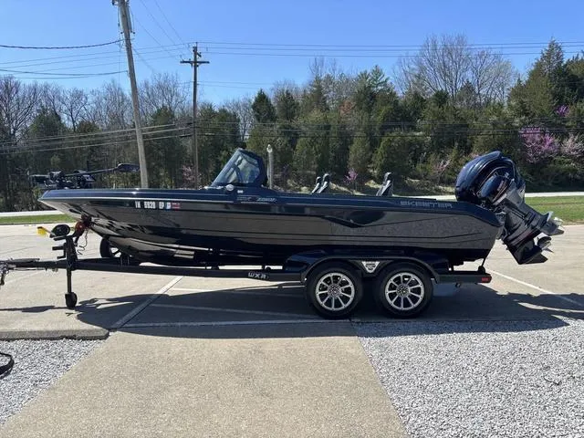 Slide: The Image of 2024 Skeeter WXR2060 F boat on trailer in parking lot, surrounded by trees. - 13