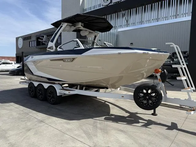 Slide: The Image of 2025 Tigé 23ZX boat on trailer, parked outdoors near a modern building. - 2
