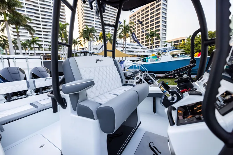 Slide: The Image of 2025 Yellowfin 26 Hybrid boat interior with modern seating and controls, docked near palm trees. - 2