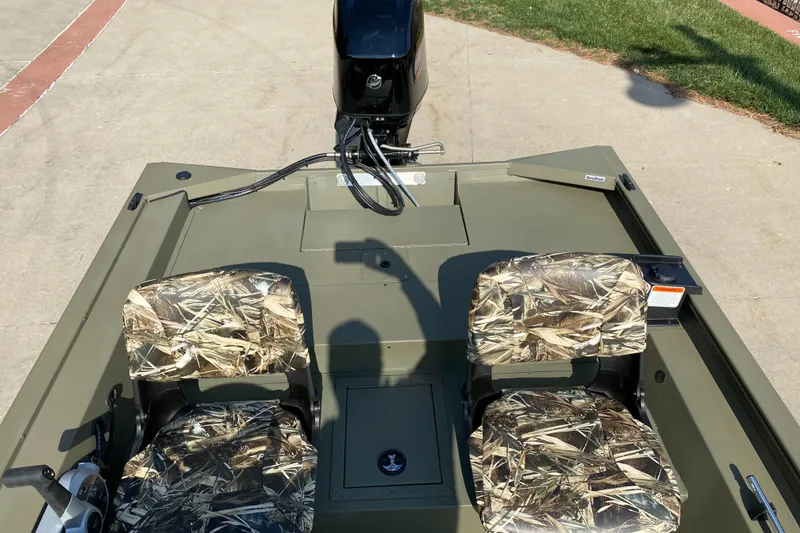 Slide: The Image of 2025 Tracker Grizzly 1754 SC boat with camo seats and motor, parked on concrete. - 5