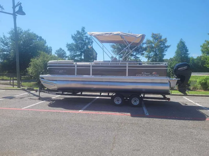 The Image of 2025 Sun Tracker SportFish 22 DLX pontoon boat on trailer in parking lot. - 0