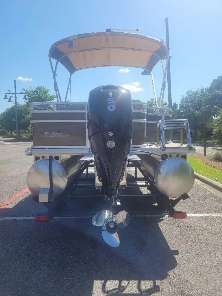 Slide: The Image of 2025 Sun Tracker SportFish 22 DLX pontoon boat parked in a lot under clear blue sky. - 2