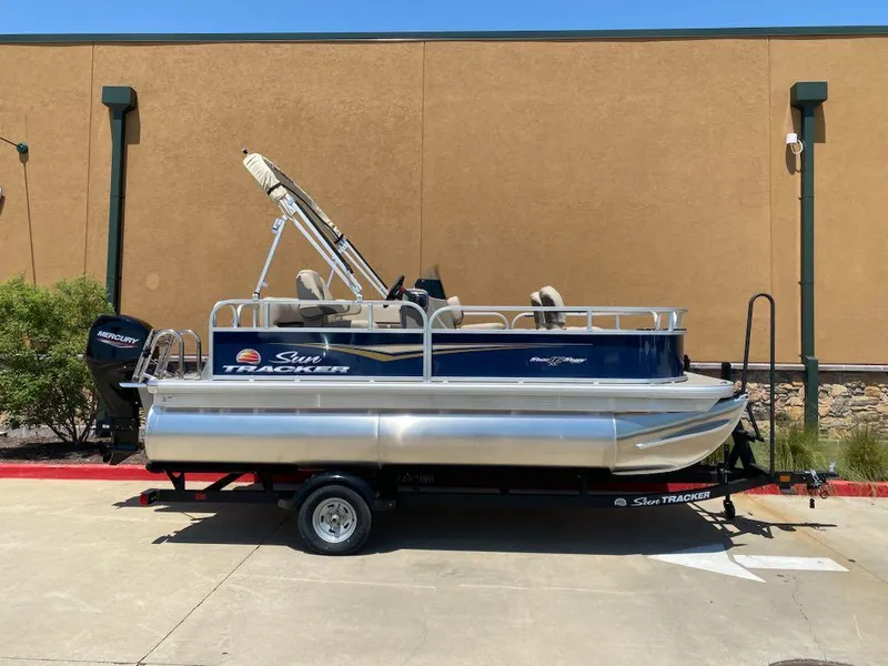 Slide: The Image of 2025 Sun Tracker Bass Buggy 16 XL Select pontoon boat on trailer, parked outdoors. - 3