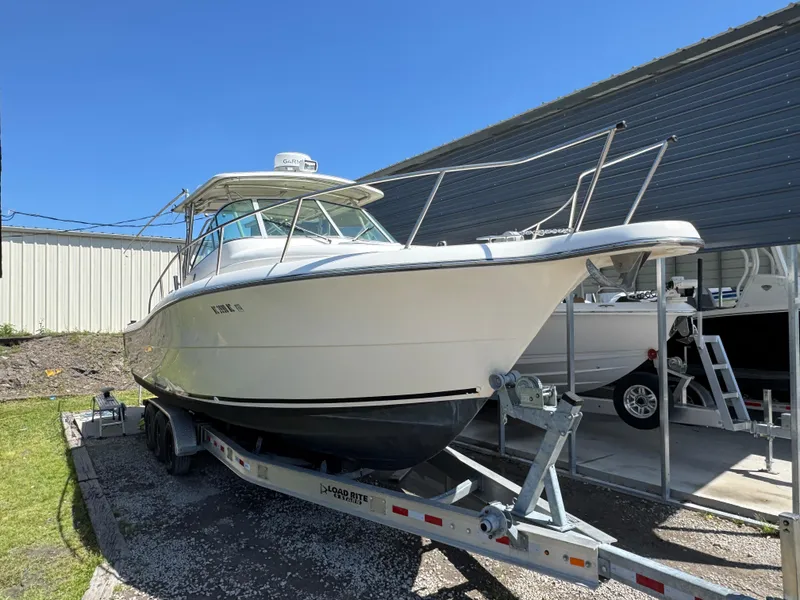 Slide: The Image of 2001 Pursuit 3070 boat on trailer, parked outdoors near a metal building. - 2