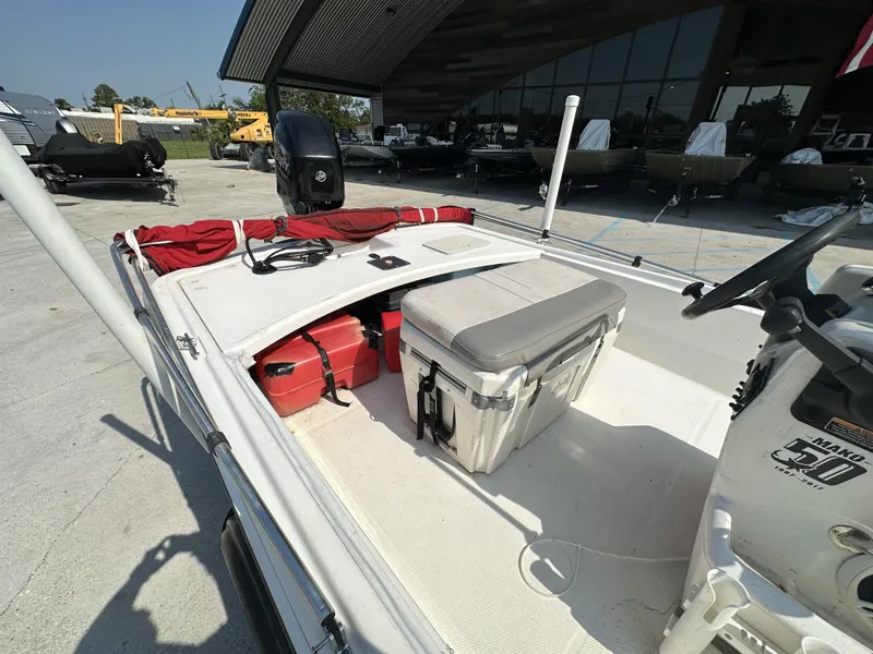 Slide: The Image of 2018 Mako 17 Pro Skiff boat with storage compartments and seating, parked outdoors. - 8