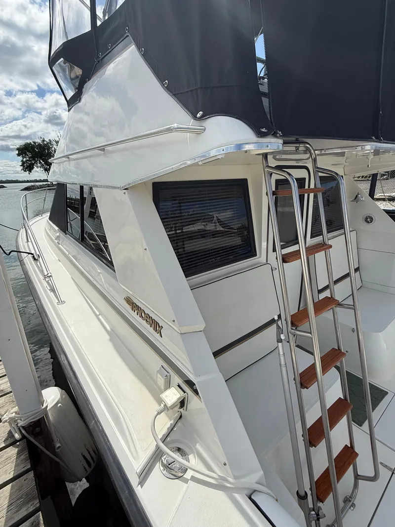 Slide: The Image of 1989 Phoenix 33 SFX boat with ladder, docked by the water under a partly cloudy sky. - 21