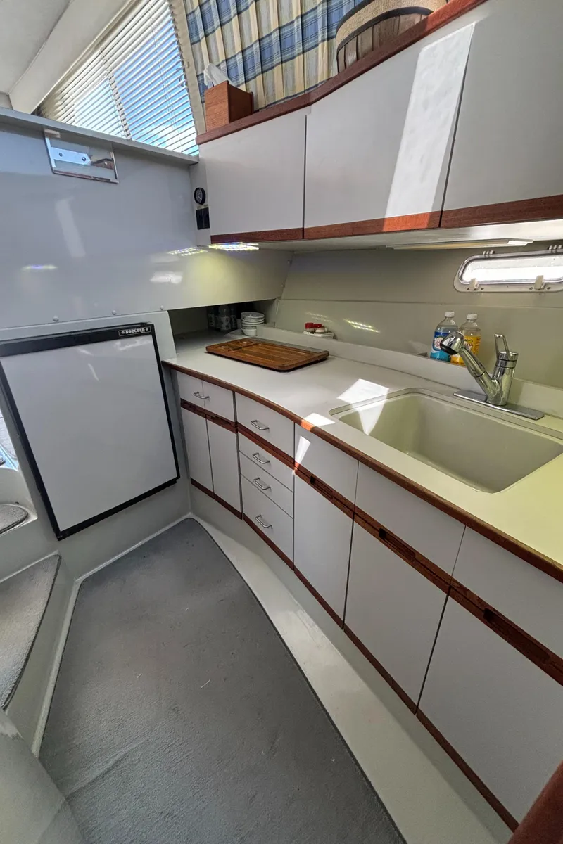 Slide: The Image of 1989 Phoenix 33 Sportfish boat kitchen with white cabinets, sink, and compact refrigerator. - 46
