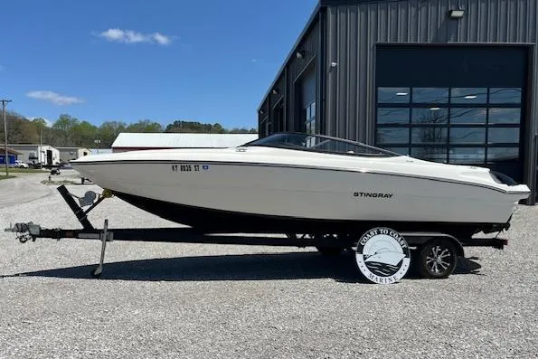 Slide: The Image of 2021 Stingray 225 SE boat on trailer, parked outside a building. - 0