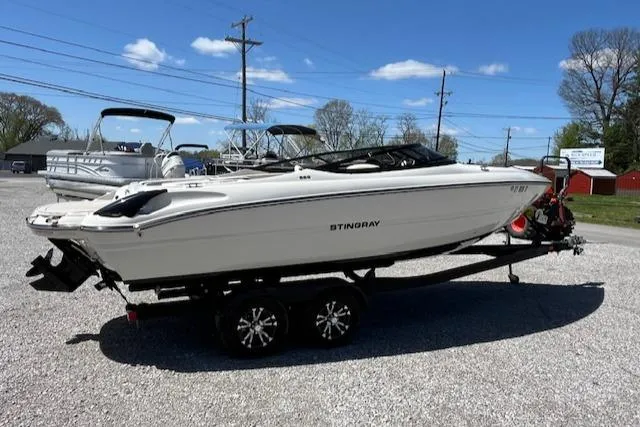 Slide: The Image of 2021 Stingray 225 SE boat on trailer in outdoor lot under clear blue sky. - 1
