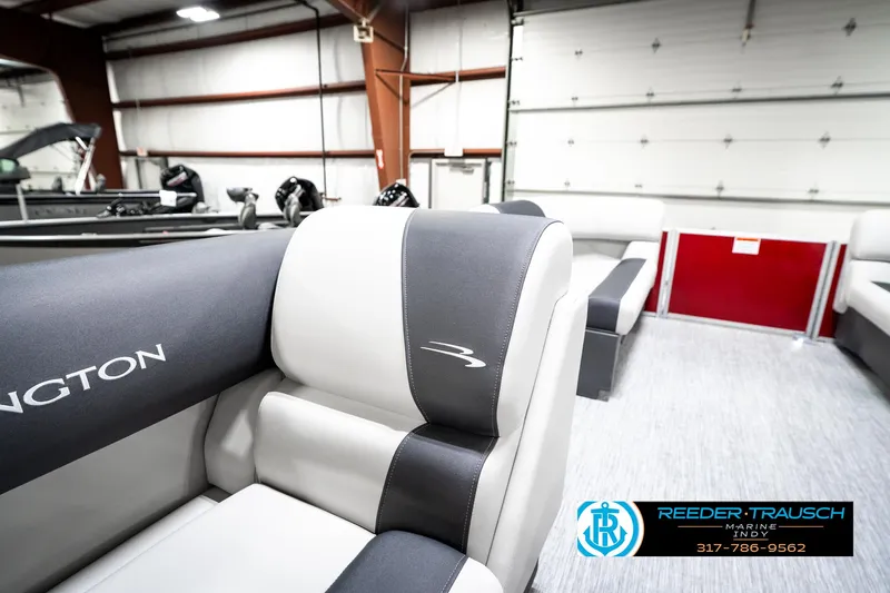 Slide: The Image of 2025 Bennington 20 SL pontoon boat interior with gray and black seating in a showroom. - 23