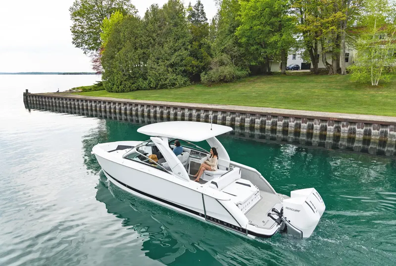 Slide: The Image of 2025 Four Winns H9C boat cruising on a serene lake near a lush, green shoreline. - 2