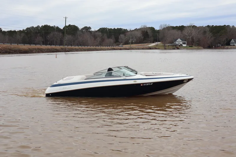 The Image of 1996 Cobalt 220 boat cruising on a calm lake with wooded shoreline. - 1