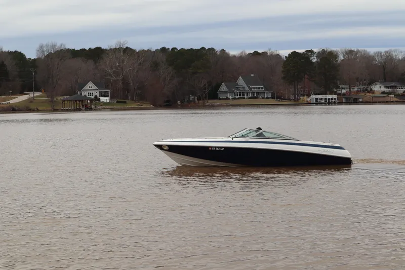 Slide: The Image of 1996 Cobalt 220 boat cruising on a calm lake with houses in the background. - 3