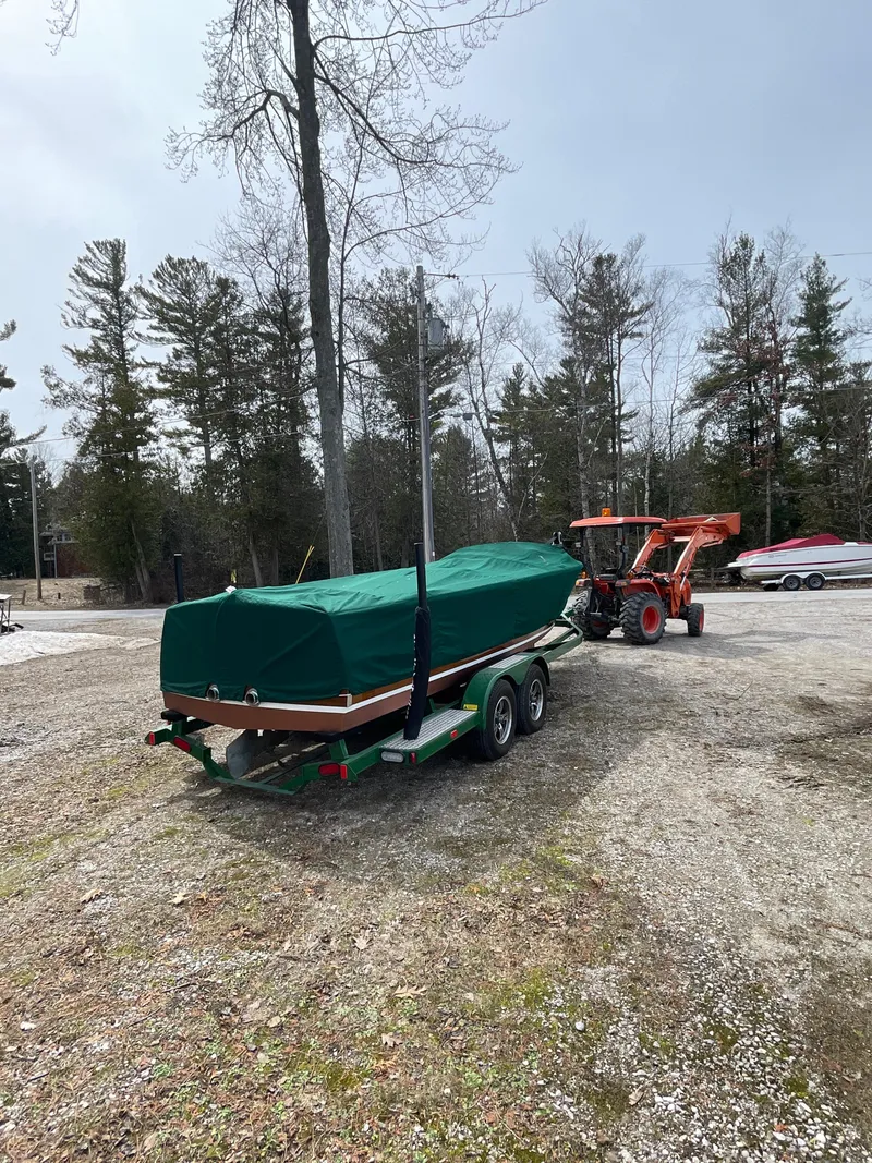 Slide: The Image of 1951 Hacker-Craft 22 Utility boat covered on trailer, towed by tractor in wooded area. - 14