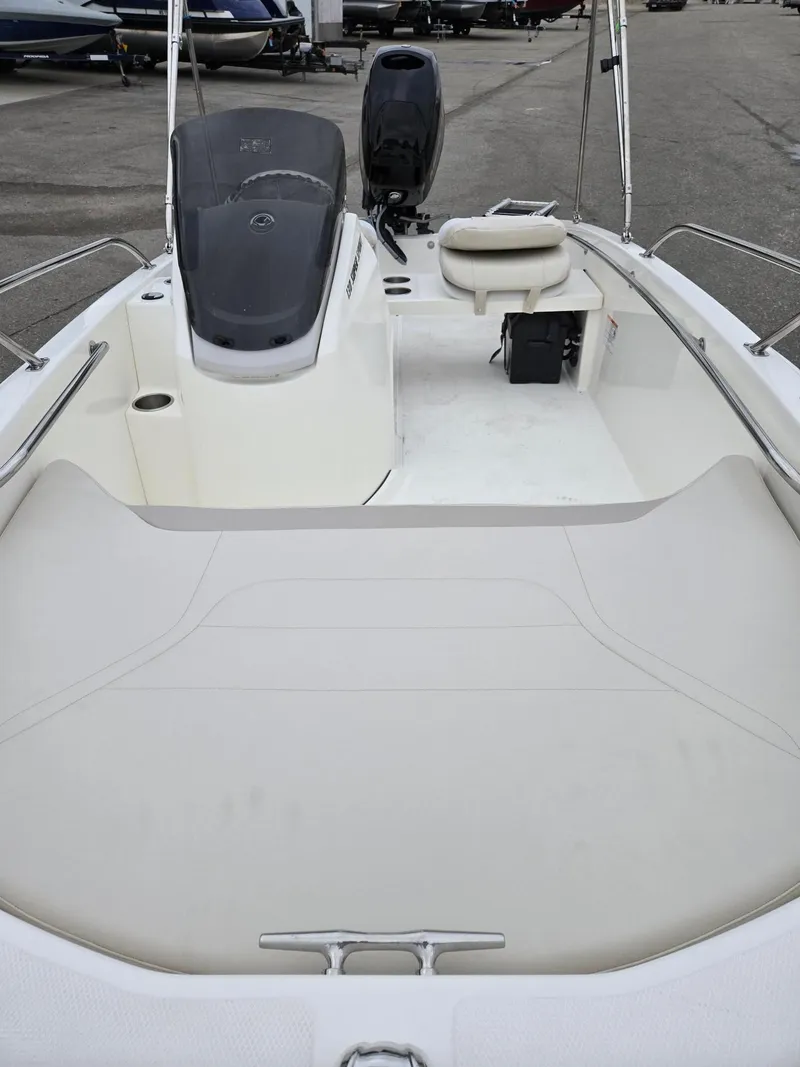 Slide: The Image of 2025 Boston Whaler 130 Super Sport interior, featuring seating and console, in a marina setting. - 7