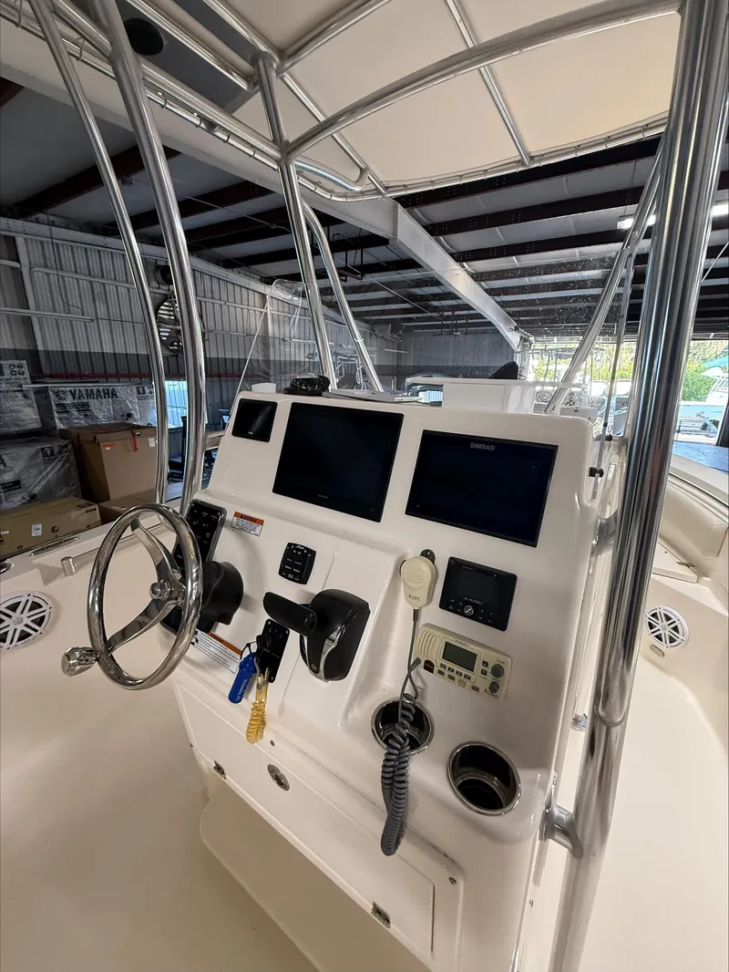 Slide: The Image of 2022 Cobia 237 CC boat console with steering wheel and navigation screens in a marina. - 11