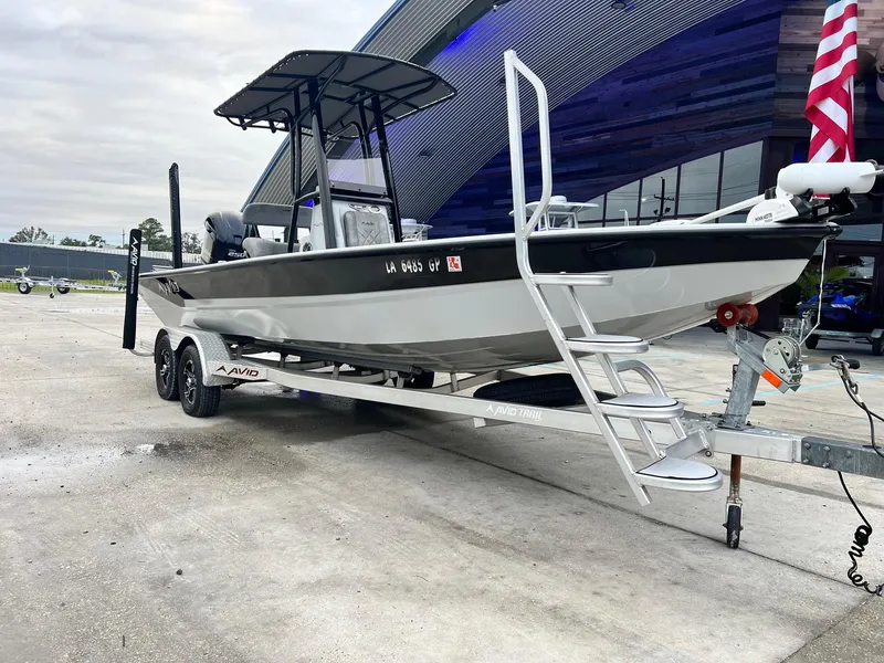 Slide: The Image of 2023 Avid 23 Mag boat on trailer, parked outdoors near a modern building. - 11