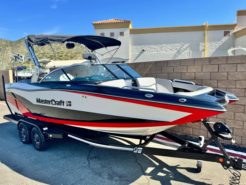 Slide: The Image of 2018 MasterCraft XT22 boat with sleek design, parked on a trailer, sunny day backdrop. - 1