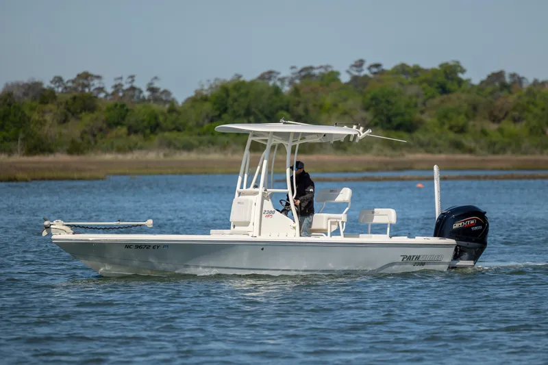 Slide: The Image of 2023 Pathfinder 2300 HPS boat cruising on a calm lake with trees in the background. - 0