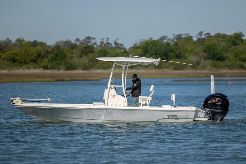 Slide: The Image of 2023 Pathfinder 2300 HPS boat cruising on a calm lake with lush green shoreline. - 1