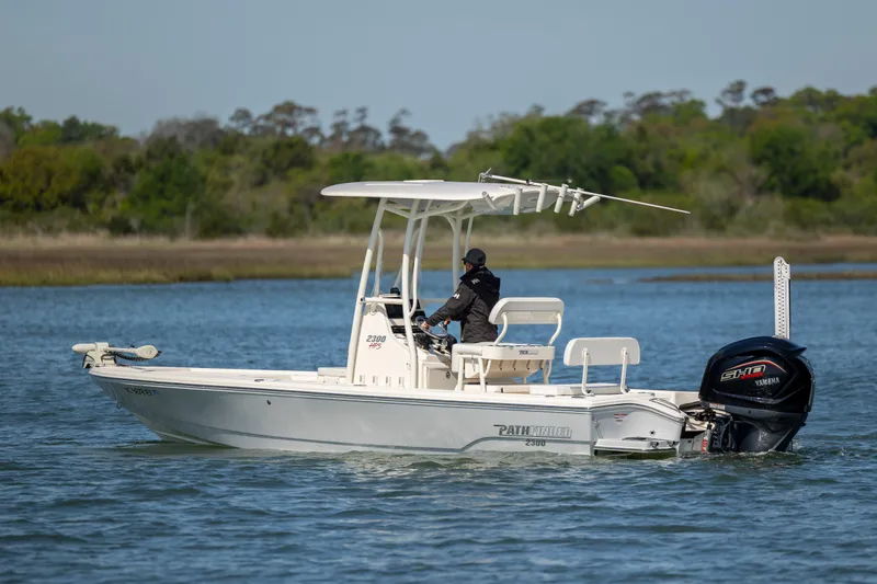 Slide: The Image of 2023 Pathfinder 2300 HPS boat cruising on a calm lake with lush greenery. - 2