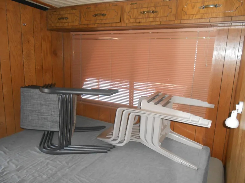 Slide: The Image of 1984 Boatel Hercules interior with stacked chairs on bed, wood paneling, and window blinds. - 17