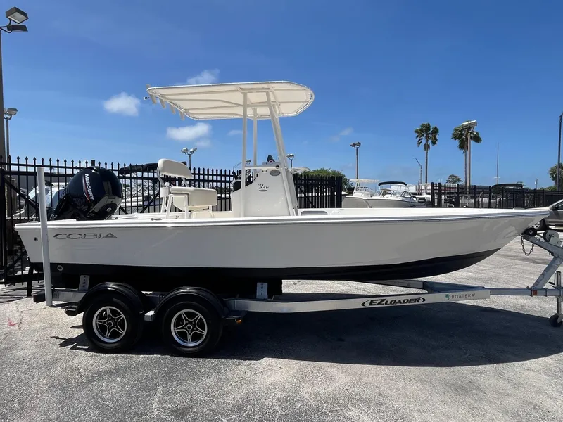 The Image of 2021 Cobia 21 Bay boat on trailer, parked outdoors under clear blue sky. - 0