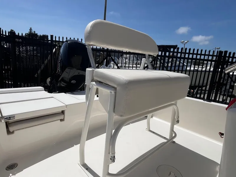 Slide: The Image of 2021 Cobia 21 Bay boat with white seating and outboard motor, docked near a fence. - 12