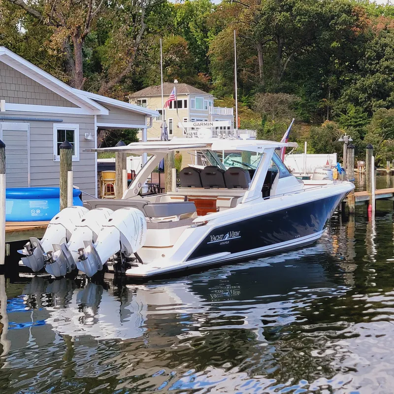 Slide: The Image of 2021 Tiara Yachts 38 LS docked near a waterfront house with lush greenery. - 3