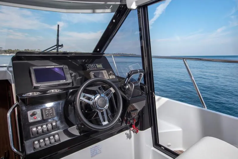 Slide: The Image of 2025 Jeanneau NC1095 Coupe helm with ocean view, featuring modern navigation controls. - 12