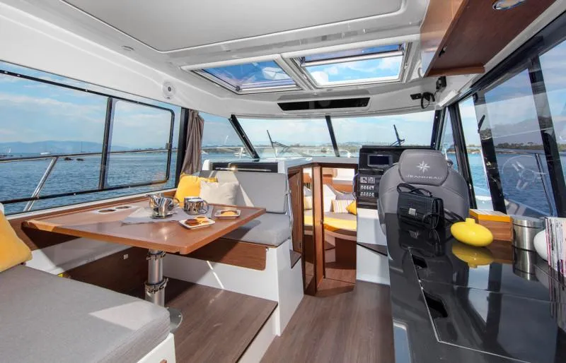 Slide: The Image of 2025 Jeanneau NC1095 Coupe interior with dining area, helm, and panoramic windows. - 9