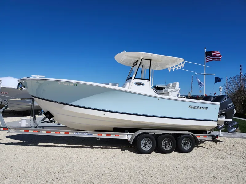 Slide: The Image of 2020 Regulator 25 boat on trailer, clear sky, American flag in background. - 0