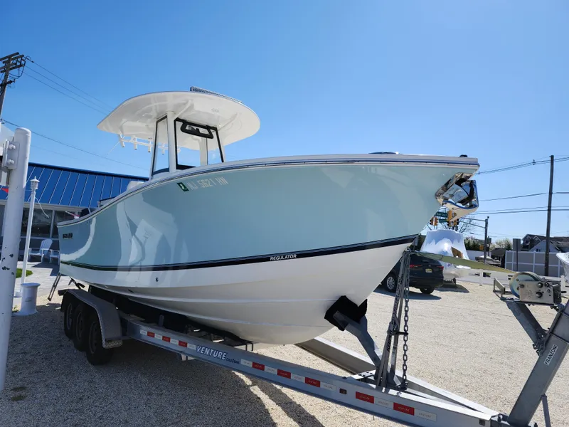 Slide: The Image of 2020 Regulator 25 boat on trailer, light blue hull, parked outdoors under clear sky. - 3