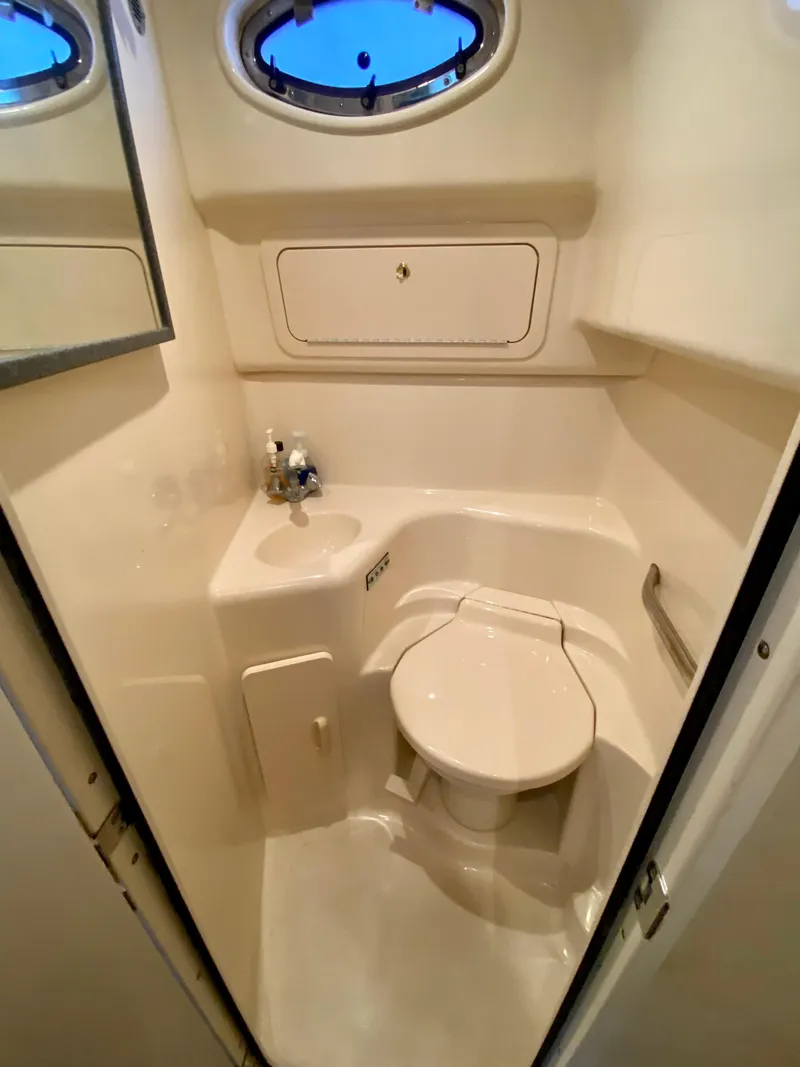 Slide: The Image of 1997 Sea Ray 400 Sundancer bathroom with compact design, featuring a toilet, sink, and porthole window. - 25