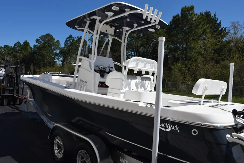 Slide: The Image of 2025 BlackJack 256 Coastal boat on trailer, parked outdoors with trees in background. - 7
