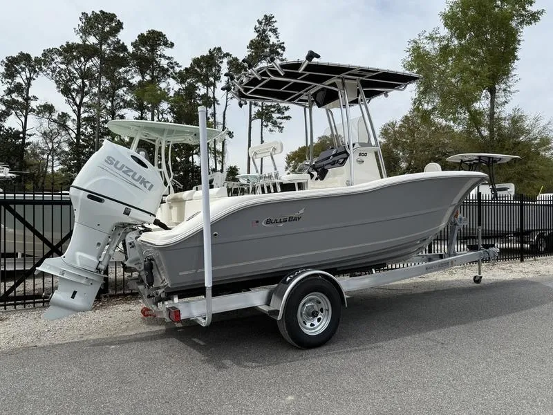 Slide: The Image of 2025 Bulls Bay 200 CC boat on trailer with Suzuki outboard motor, parked outdoors. - 2