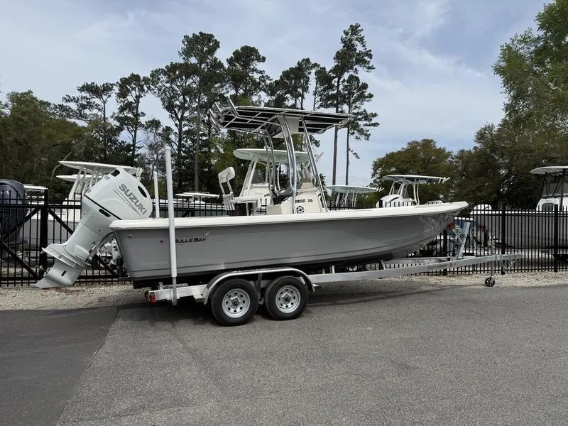 Slide: The Image of 2025 Bulls Bay 2200 XS boat on trailer, parked outdoors near trees and fence. - 2