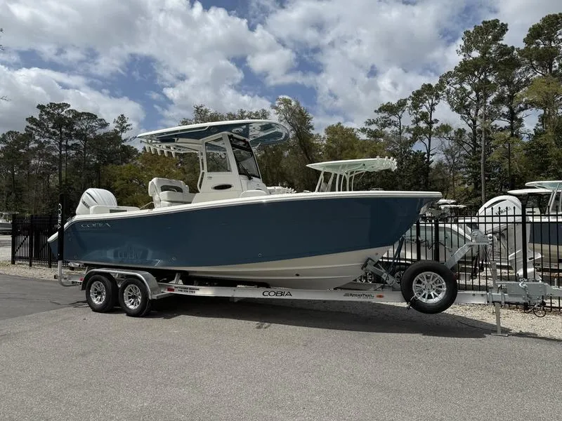 Slide: The Image of 2025 Cobia 240 Center Console boat on trailer, parked outdoors under cloudy sky. - 0