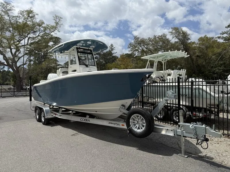 Slide: The Image of 2025 Cobia 240 Center Console boat on trailer, parked outdoors near trees and fence. - 1