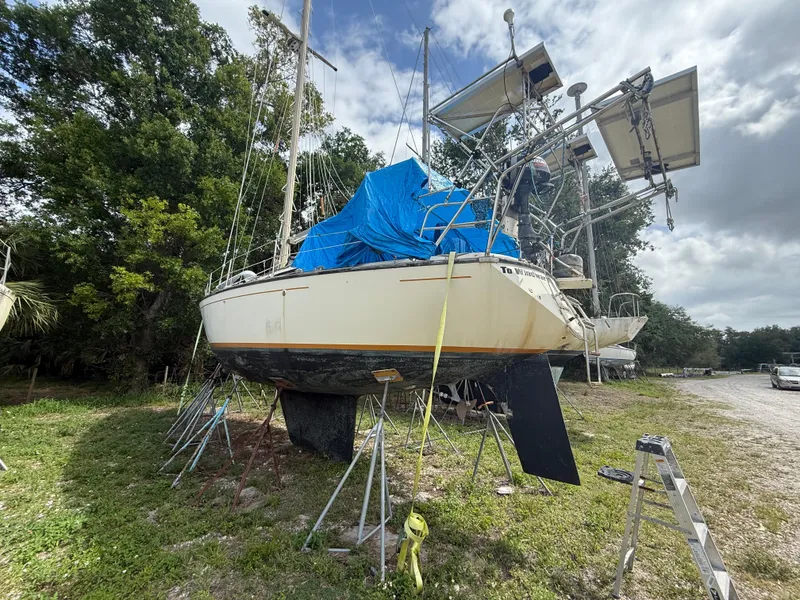 Slide: The Image of 1981 S2 11A sailboat on land, covered with blue tarp, surrounded by trees and equipment. - 7
