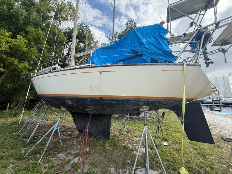 Slide: The Image of 1981 S2 11A sailboat on stands, covered with blue tarp, outdoors. - 8