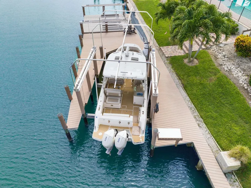 Slide: The Image of Boston Whaler 320 Vantage 2022 docked, aerial view, turquoise water, lush greenery nearby. - 3