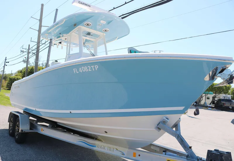 Slide: The Image of 2023 Cobia 240 CC boat on trailer, light blue hull, parked outdoors. - 2