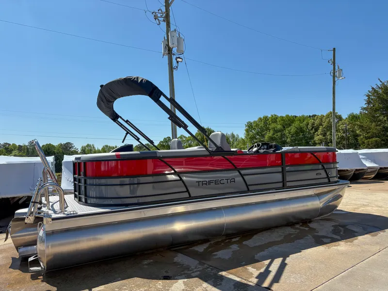 Slide: The Image of 2025 Trifecta 22RF CS pontoon boat with red accents, docked outdoors under clear blue sky. - 1